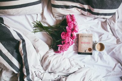 An image of some flowers, a book, and coffee on a bed